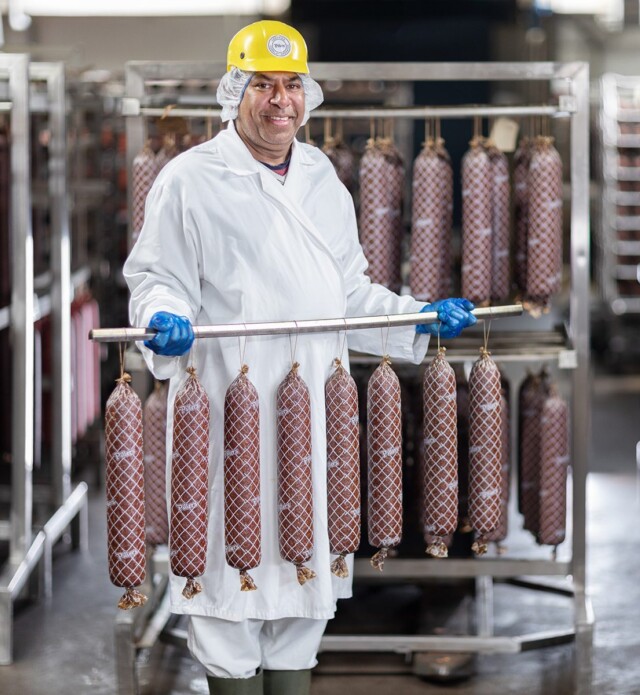 Employee holding rack of drying salami